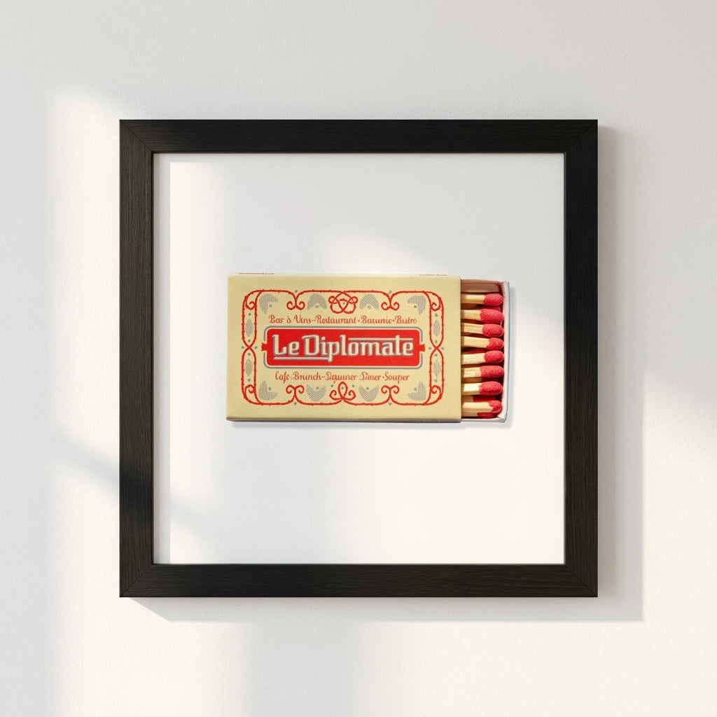 Macro shot showcasing the textured paper and quality frame of the 'Le Diplomate' poster, with warm lighting highlighting gloss and matte details on a white background.
