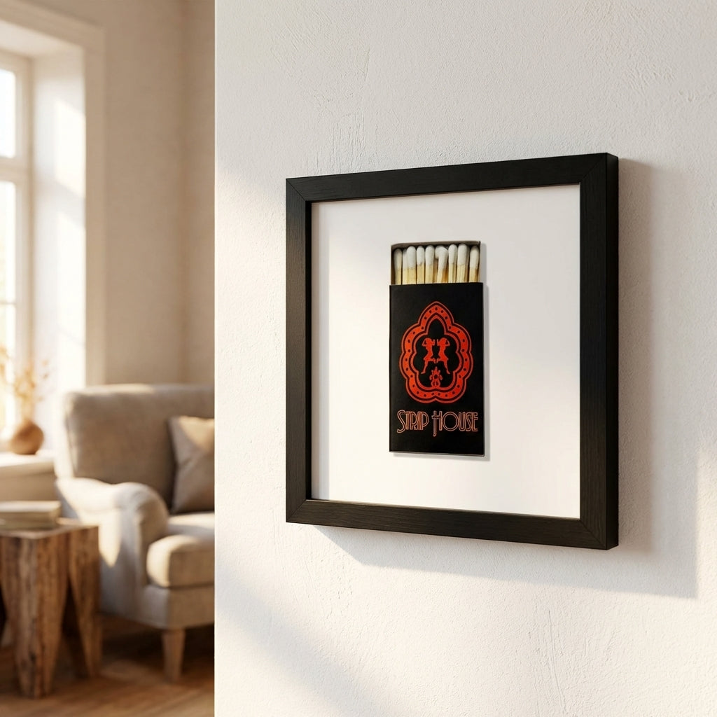 Full view of 'Strip House Matchbox' framed print on a white wall in a warm, inviting living room with natural light highlighting the wooden frame.