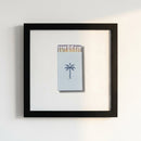 Full view of 'Island Provisions' framed print on a white wall in a warm, inviting space with natural sunlight highlighting the matte black frame and high-quality paper.