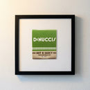 High-quality framed 'DeNucci’s' poster on white wall with glossy and matte textures, soft natural light highlighting details in a cozy setting.