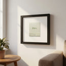 High-resolution image of Elio’s Framed Print hanging on a white wall in a cozy environment, showcasing its glossy and matte paper finish with a wood frame.