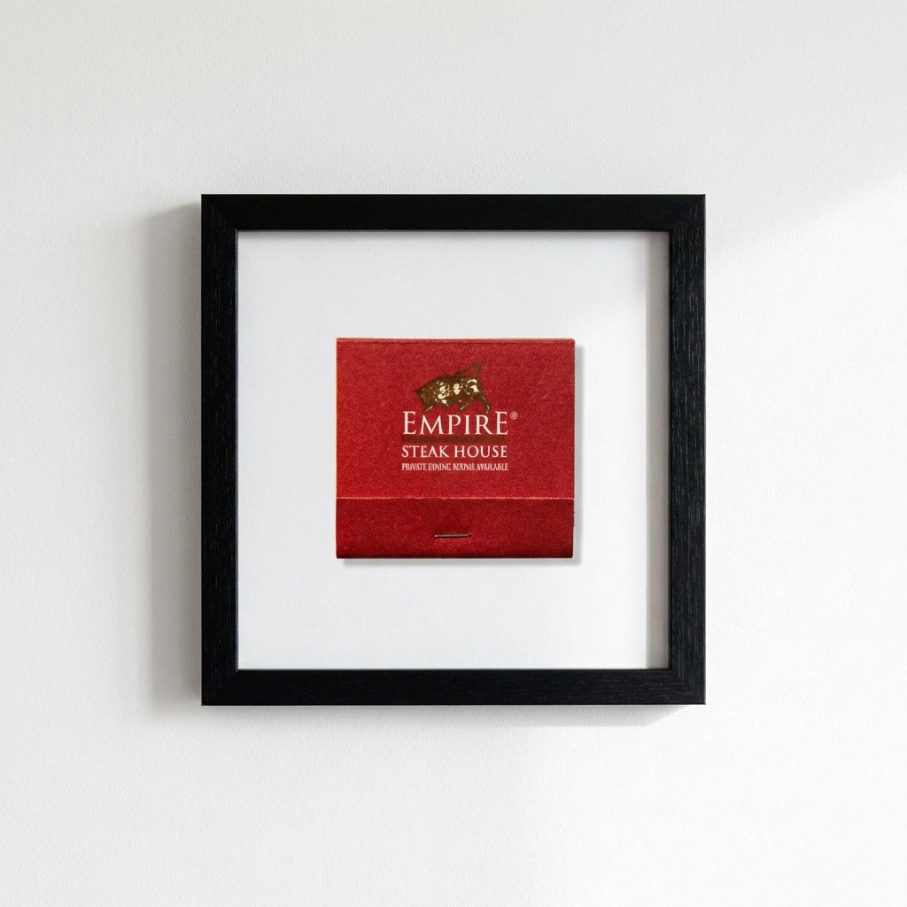 High-resolution shot of Empire Steakhouse framed print on wall, emphasizing black wood frame and detailed textured paper in warm natural light.