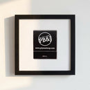 Vibrant 'PB&J's Chicago' poster in a glossy black wood frame hanging on a white wall, illuminated by soft natural daylight.