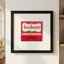 Full-body view of Gene & Georgetti framed print on white wall, featuring warm lighting, detailed wooden frame, and glossy matte paper surface in cozy setting.