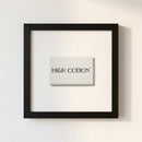 Framed high cotton print hanging on a white wall in a cozy indoor setting with warm lighting.