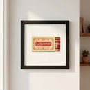 Highly detailed photograph of the 'Le Diplomate' poster framed in ayous wood, hanging on a white wall in a warm, cozy living room setting with soft natural light.