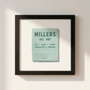 Professional shot of Millers All Day Framed Print on white wall in cozy living room with warm natural lighting, highlighting glossy and matte textures and wooden frame.