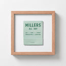 Studio-style portrait of Millers All Day Framed Print mounted on white wall with warm LED lighting, emphasizing textured paper and wooden frame in a realistic living room.
