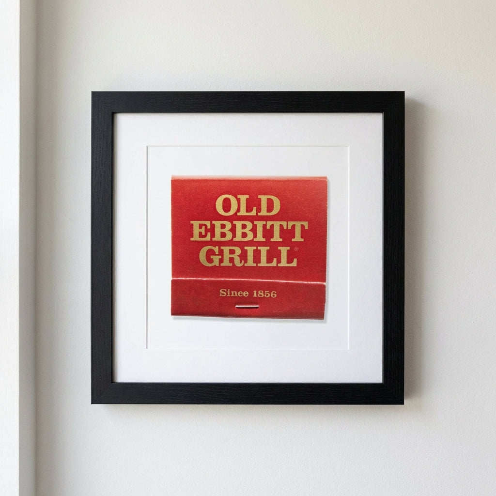 Realistic image of 'Old Ebbitt Grill' framed poster in minimalistic cozy room with natural light highlighting paper and wood frame.