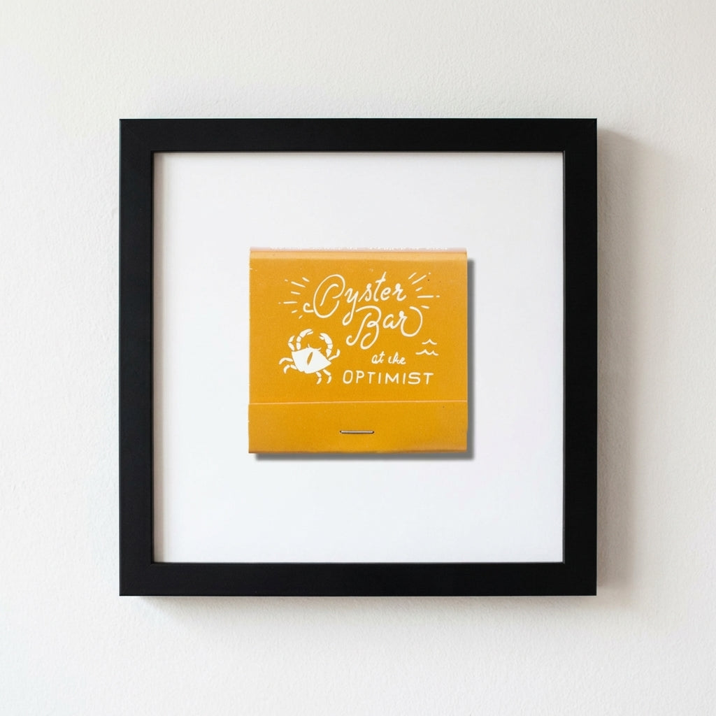 Modern Oyster Bar Framed Print hanging on a white wall in a stylish home, with warm lighting highlighting the textured matte paper and black wooden frame.