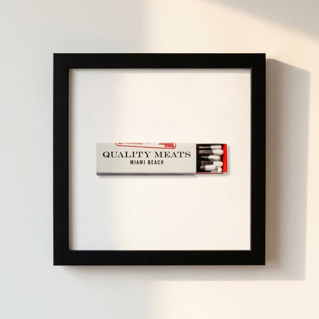 14x14 inch white frame of Quality Meats print with glossy matte finish mounted on a wall, illuminated by warm light.