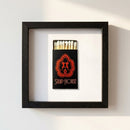 Framed 'Strip House Matchbox' print hanging on a white wall in a cozy living room with warm natural light, showcasing textured wooden frame.
