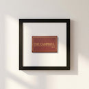Framed Campbell Bar Matchbox print hanging on a white wall in a cozy, warmly lit interior with natural light.