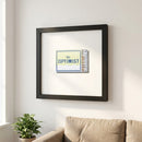 A framed print of The Optimist hanging on a wall in a warm, inviting living room with natural sunlight and soft shadows.