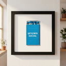 Highly detailed 'Uptown Social' print framed in natural ayous wood, showcasing micro-texture details with soft natural lighting on a white wall.
